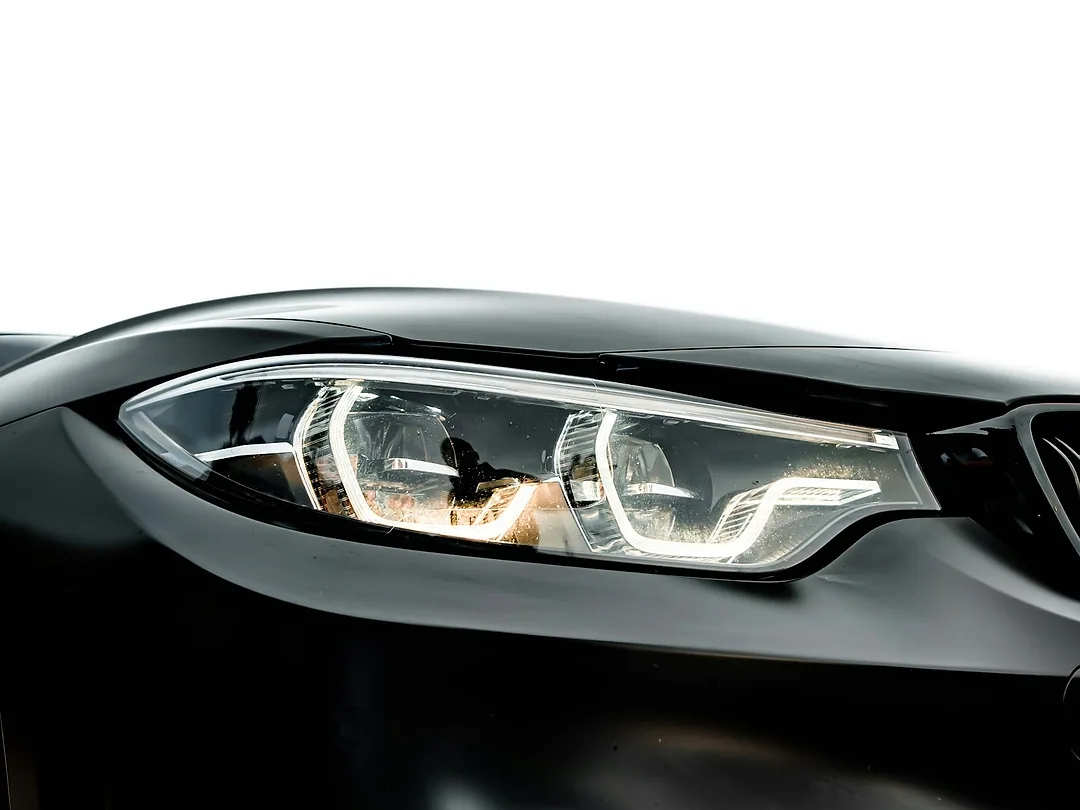 A clear LED headlight on a black car, against white