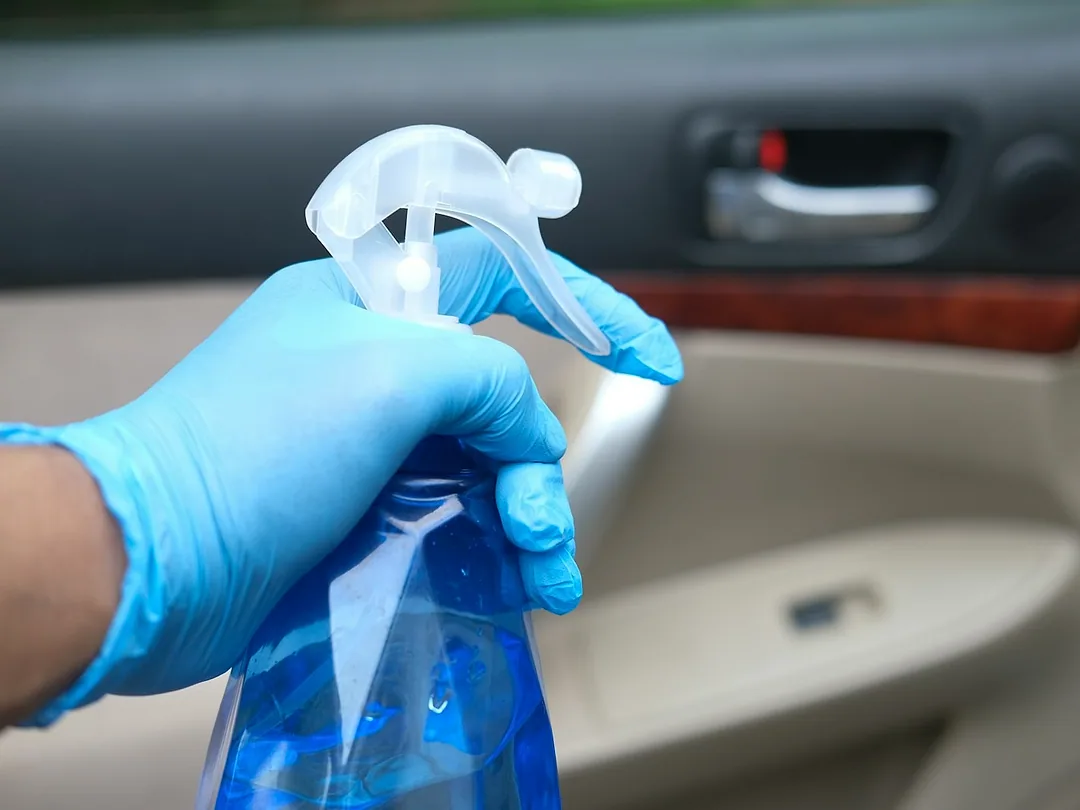A gloved hand spraying cleaner onto a car's door trim